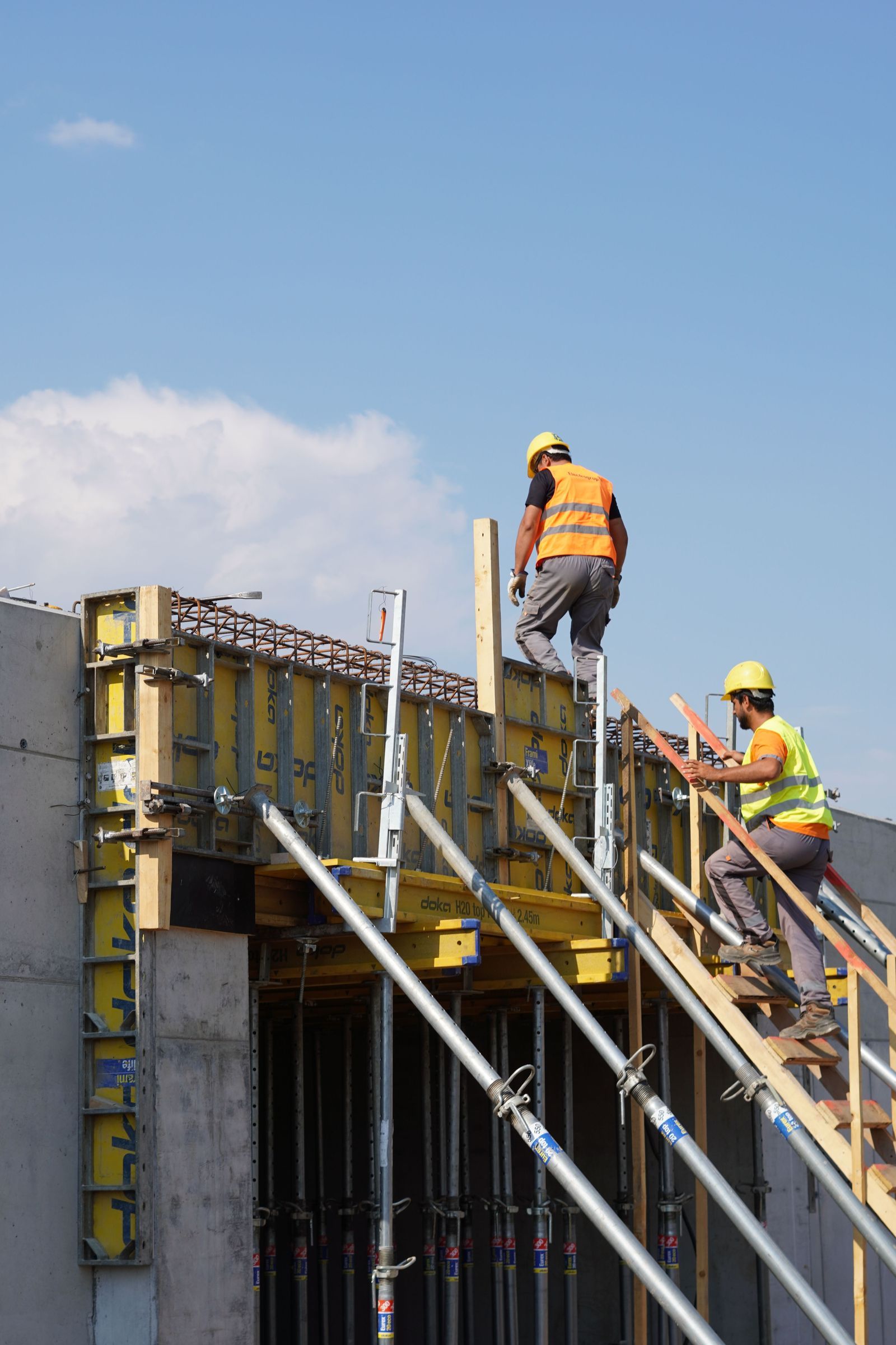 Two workers in hard hats and hi-vis vests setting wall formwork on a commercial build